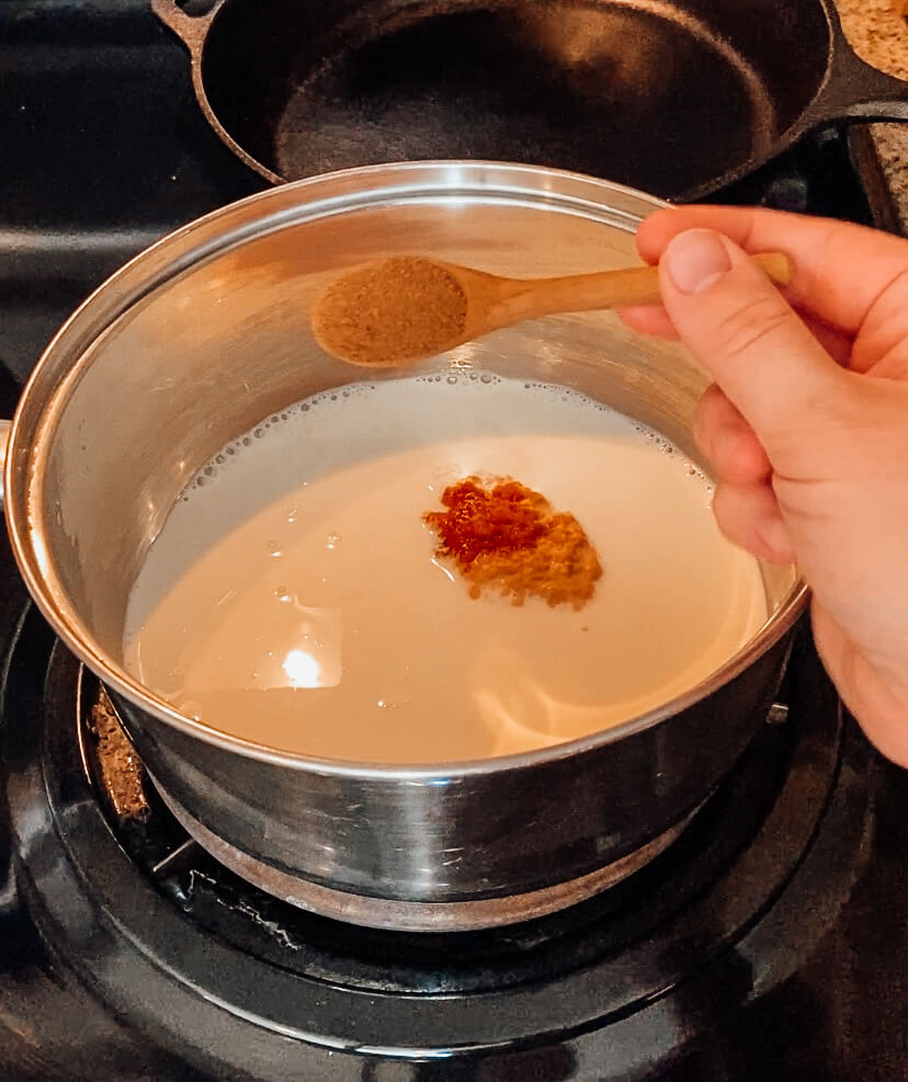 hand pouring pumpkin pie spice into a saucepan