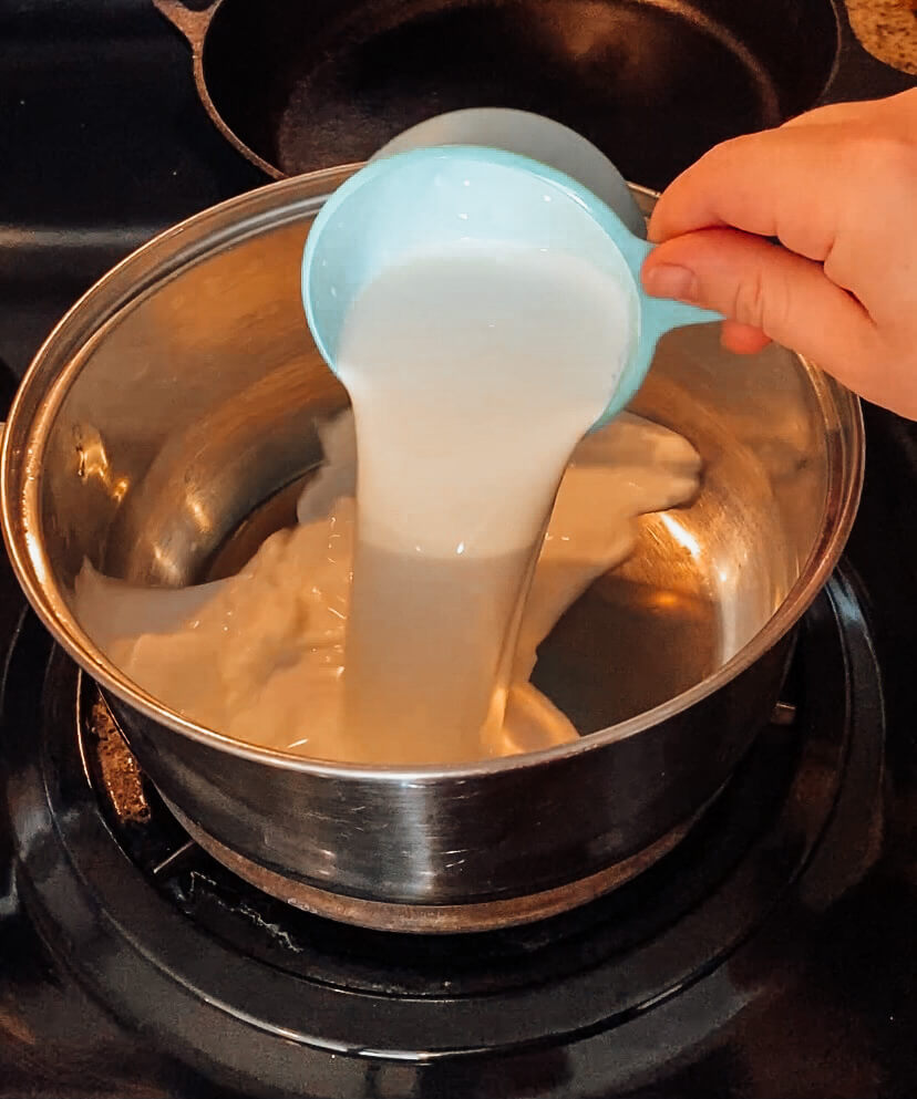 hand pouring half & half into a saucepan