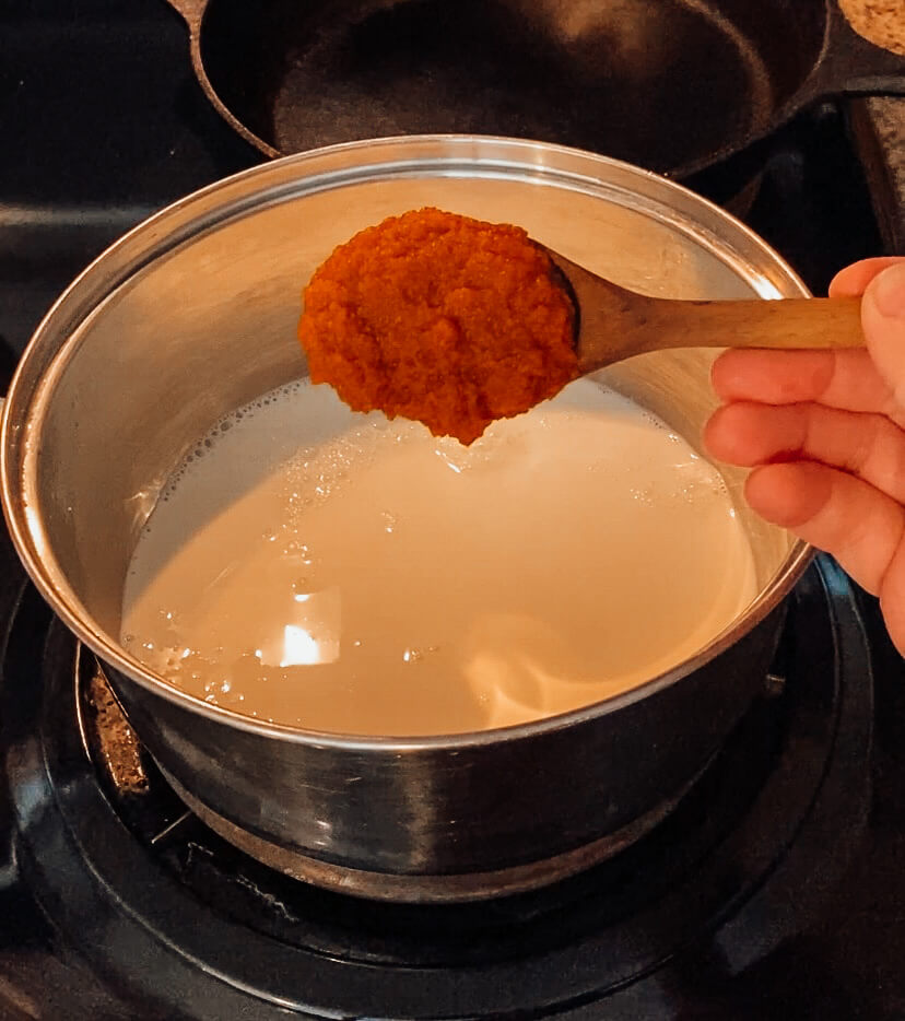 hand pouring pumpkin puree into saucepan