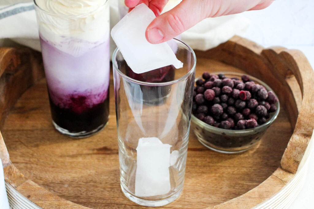 adding ice to a tall glass to make blueberry Italian cream soda